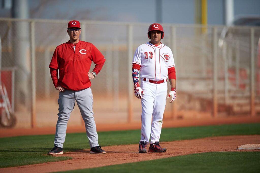 Two baseball players standing on a field with one of them holding his hands in his pockets.