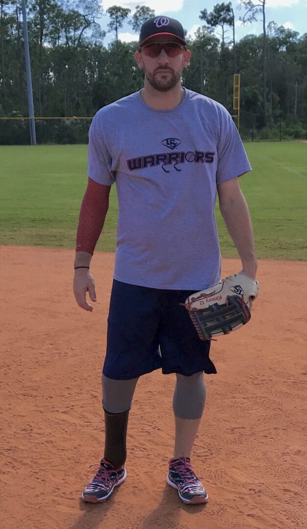 A man in grey shirt holding baseball glove on dirt field.