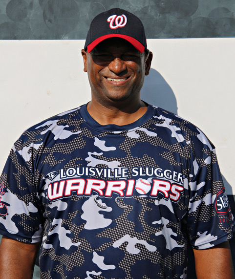 A man in camouflage shirt and hat standing next to wall.