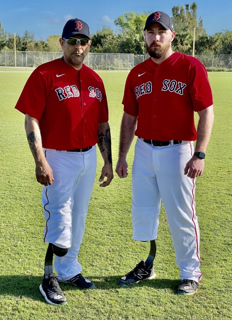 Two baseball players standing on a field with one of them wearing red.